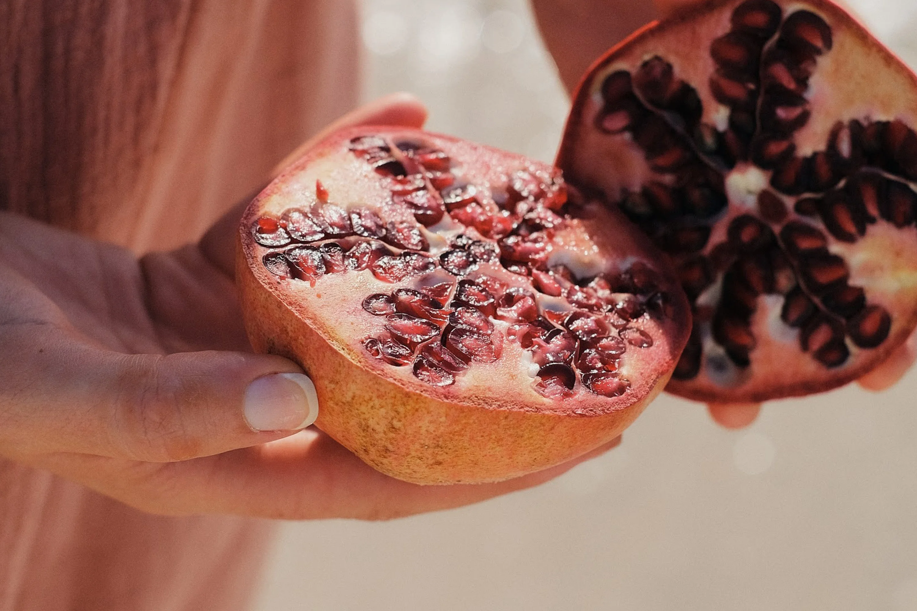 a set of hands holding a cut pomegranate